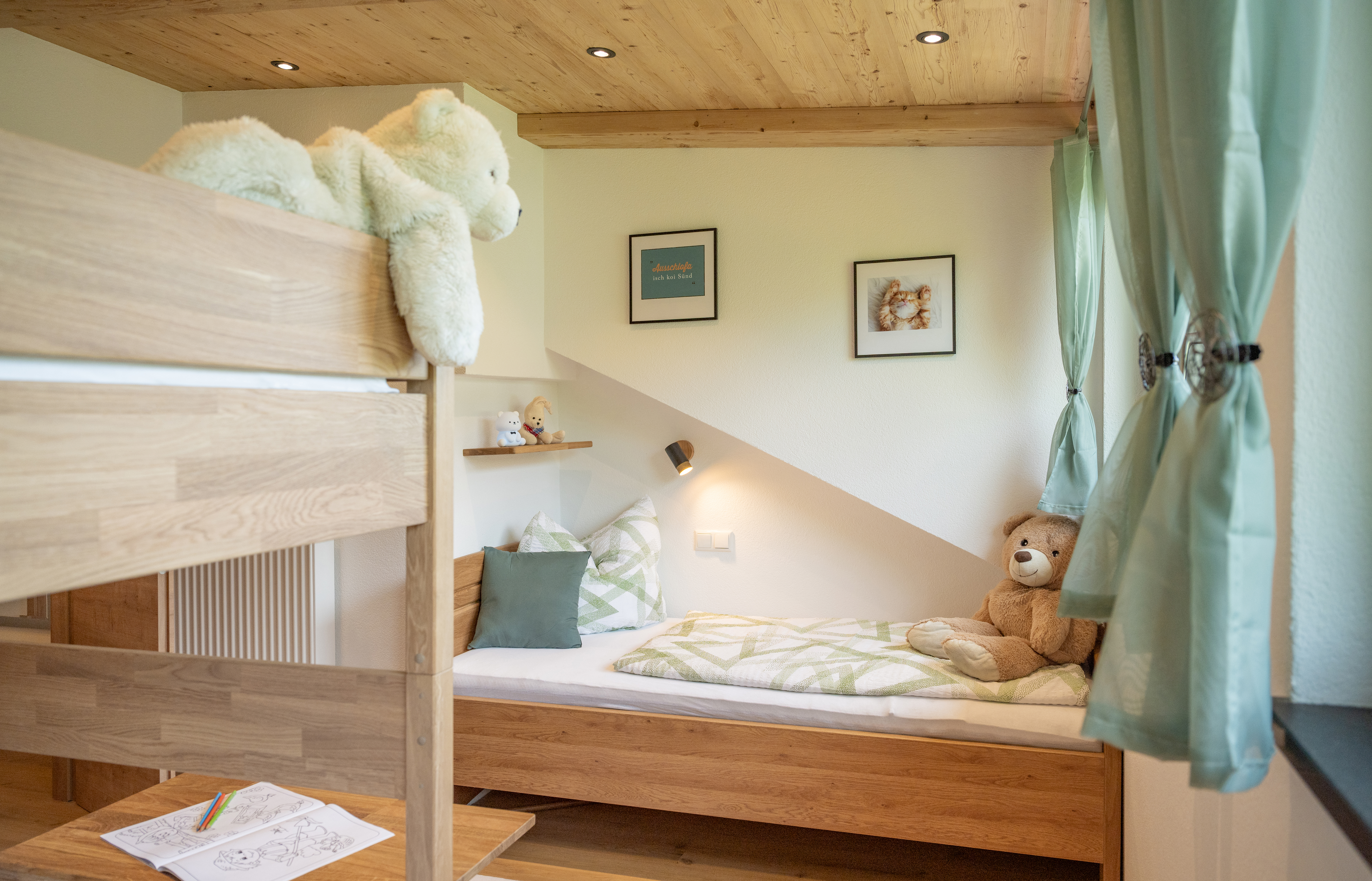 Kinderzimmer mit Holz-Hochbett, Einzelbett mit grün gemusterter Bettwäsche, Teddybären und mintgrünen Vorhängen