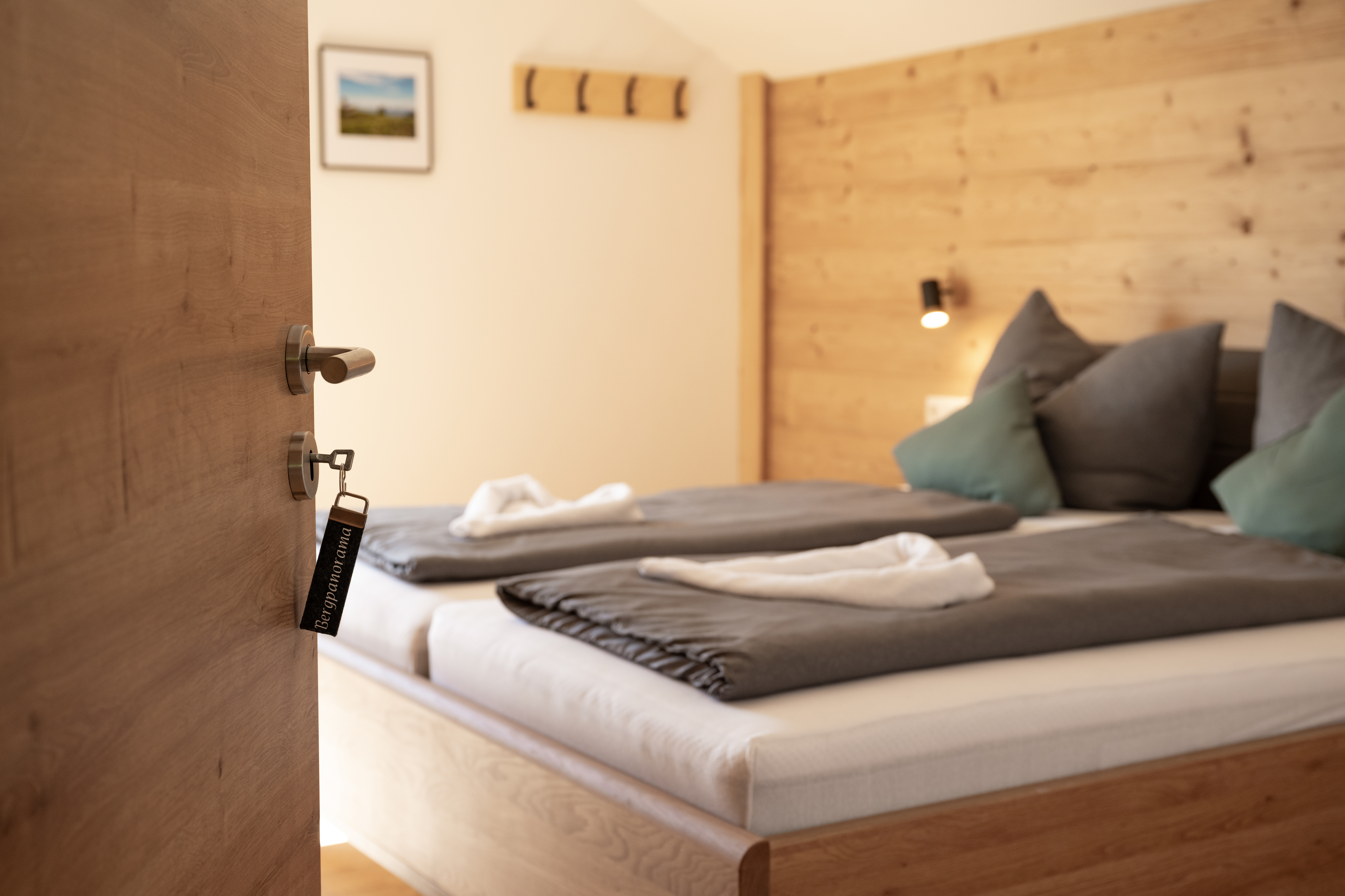 Schlafzimmer mit Doppelbett, grauer Bettwäsche und Holzwand, Blick durch die offene Tür